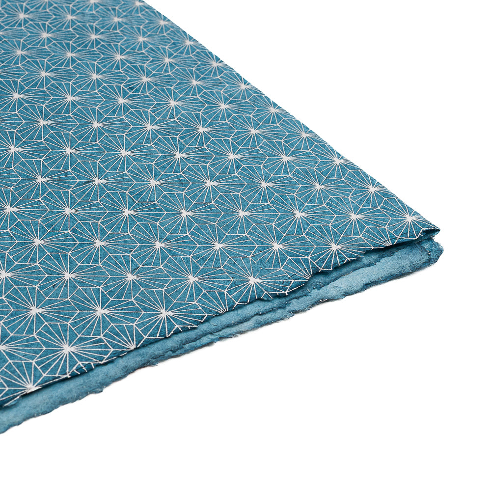 ☆ Blaues, strukturiertes Nepalpapier mit einem weißen geometrischen Sternmuster, teilweise gefaltet und vor einem weißen Hintergrund – ideal als nachhaltige Geschenkverpackung.