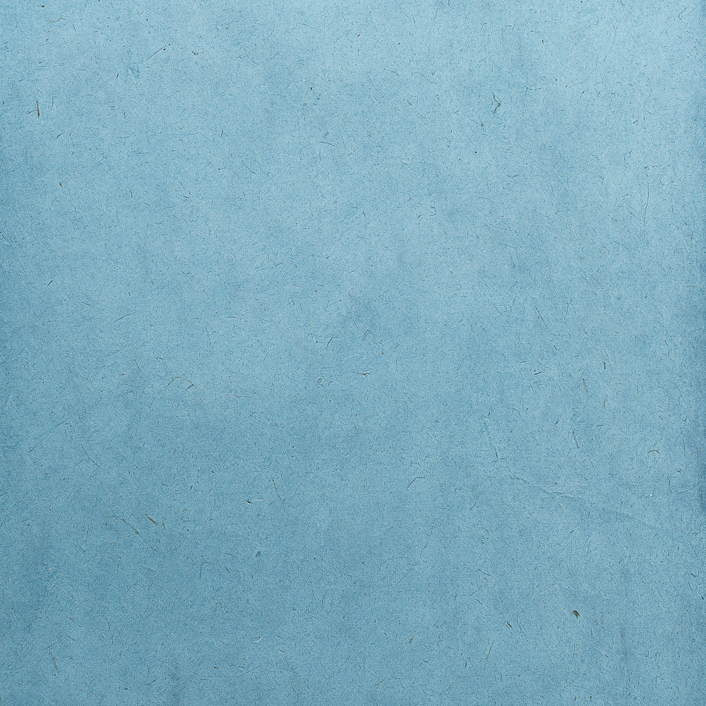 Hellblauer Nepalpapier-Hintergrund mit dezenten Fasern und kleinen Unregelmäßigkeiten, die den Charme handgeschöpfter Papiere widerspiegeln – ideal als nachhaltiges Geschenkpapier für jeden Anlass. Von ☆.