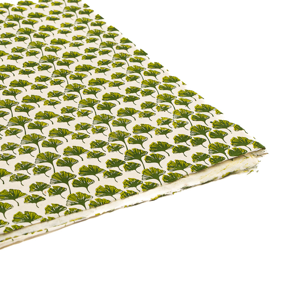 Ein Stapel ☆ Nepalpapier mit einem sich wiederholenden Muster aus grünen Ginkgoblättern auf weißem Hintergrund – ideal als nachhaltige Geschenkverpackung.