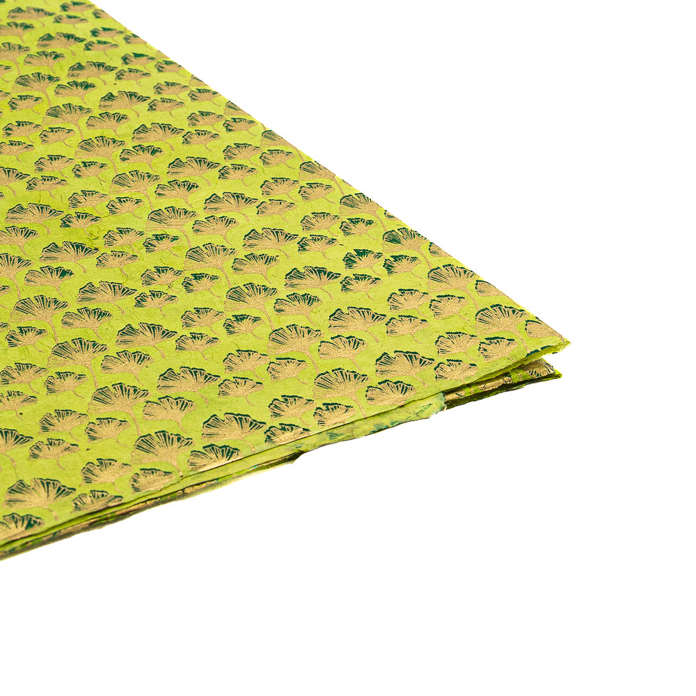 Ein gefaltetes Blatt aus ☆ nachhaltigem Papier mit grünen Mustern und eleganten, gold- und dunkelgrünen Fächermotiven – ideal für Geschenkverpackungen – vor weißem Hintergrund.