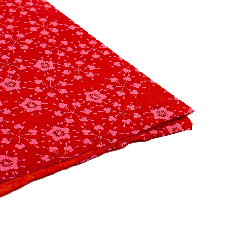 ☆ Roter Stoff mit rosa Blumenmuster, an der Ecke gefaltet und an nachhaltiges Geschenkpapier oder handgeschöpftes Papier erinnernd, vor weißem Hintergrund.