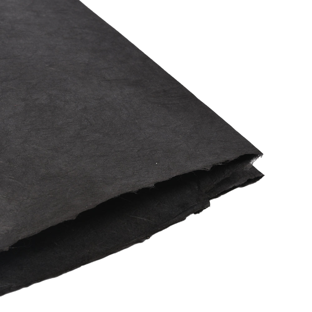 Eine Nahaufnahme von zwei grobkantigen schwarzen Nepalpapierbögen von ☆, gestapelt auf weißem Hintergrund - ideal für Buchbinden oder Geschenke Verpacken Projekte.