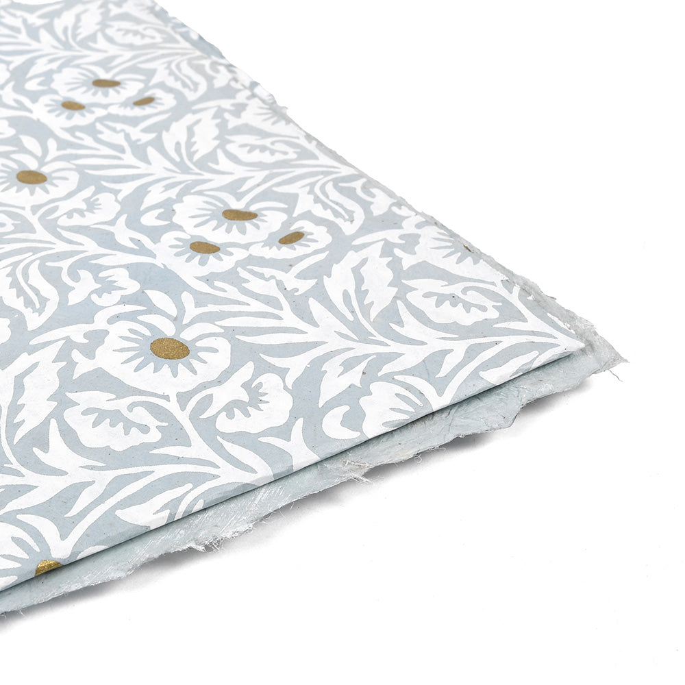 Ein ☆ Nepalpapier-Blatt mit weißem Blumenmuster und goldenen Zentren auf hellblauem Grund - perfekt für Buchbinden oder Geschenkverpackungen.