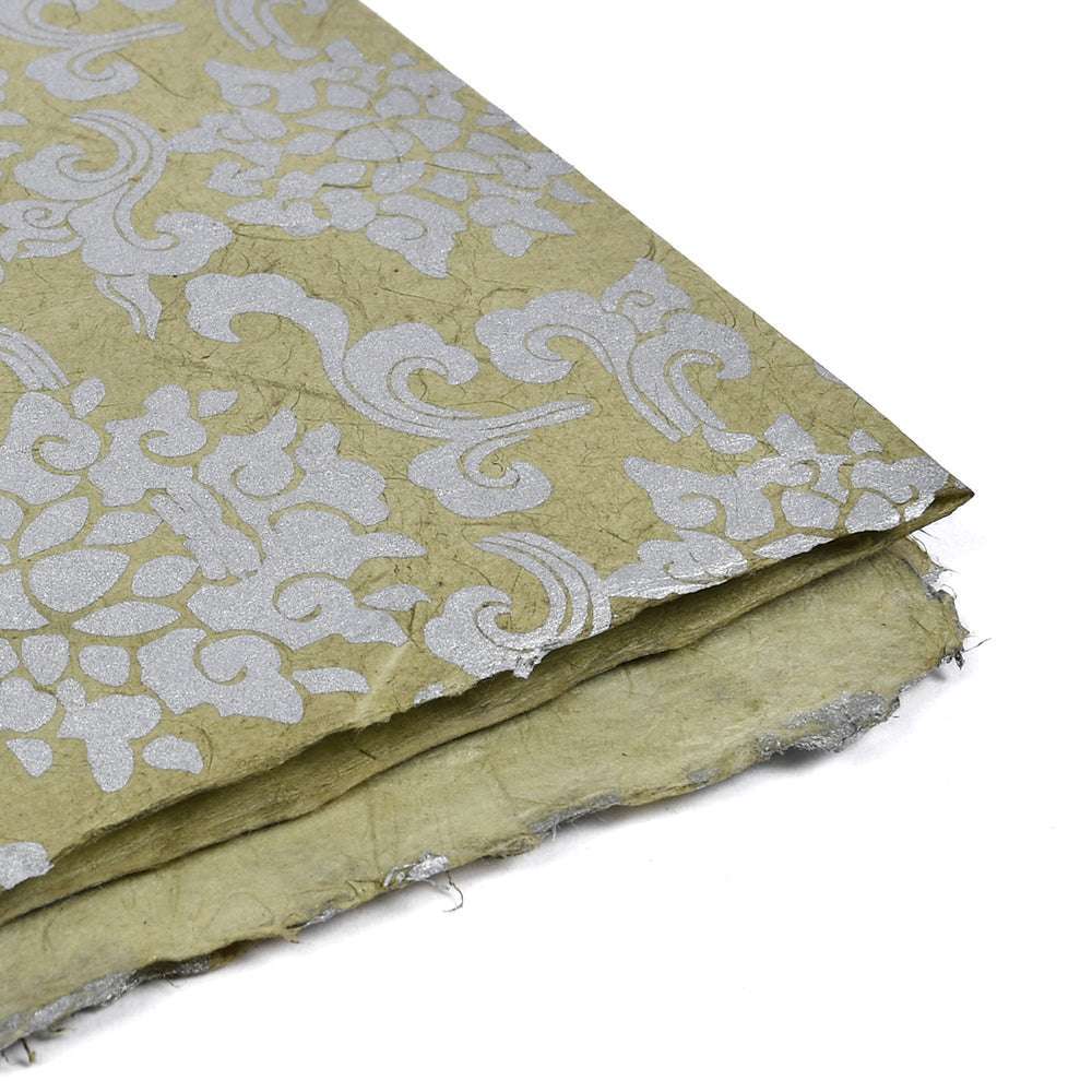 Dekoratives strukturiertes Nepalpapier mit silbernem Blumenmuster auf hellgrünem Grund und leicht ausgefransten Rändern - perfekt für Geschenkverpackungen oder Buchbindearbeiten.