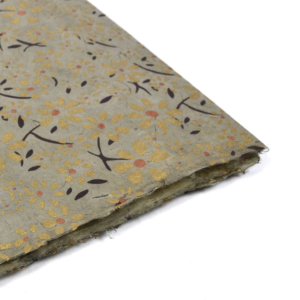 Nahaufnahme von ☆ Nepalpapier mit einem goldenen, orangefarbenen und schwarzen Blumenmuster auf einem strukturierten hellen Hintergrund - ideal für Geschenkverpackungen oder Bucheinbände.