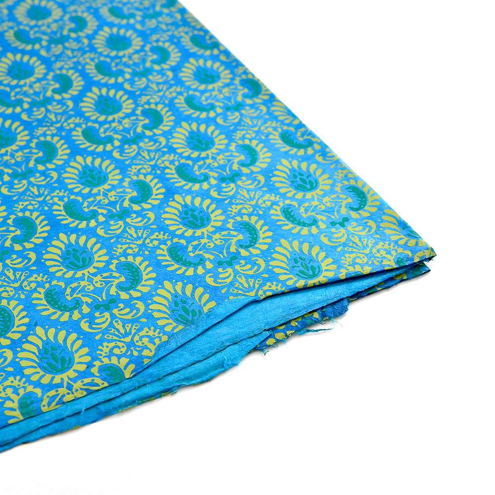 Gefalteter blauer Nepalpapier-Stoff mit verschlungenen goldenen Blumenmustern auf weißem Hintergrund - perfekt für Geschenkverpackungen oder Buchbindearbeiten.