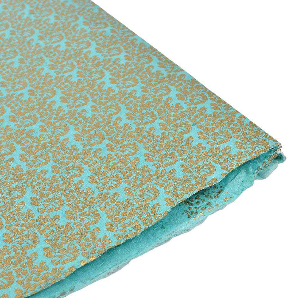 Türkisfarbenes Nepalpapier mit goldenen Blumenmustern, handgefertigt und an der Ecke leicht gefaltet, abgebildet auf weißem Hintergrund.
