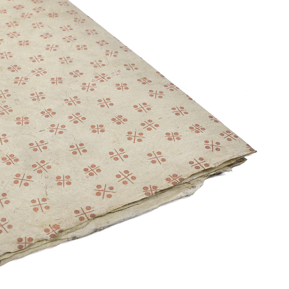 Ein Blatt beigefarbenes Nepalpapier von ☆ zeigt ein sich wiederholendes rotes geometrisches Muster, das teilweise auf weißem Papier gefaltet ist - perfekt zum Buchbinden oder Verpacken von Geschenken.