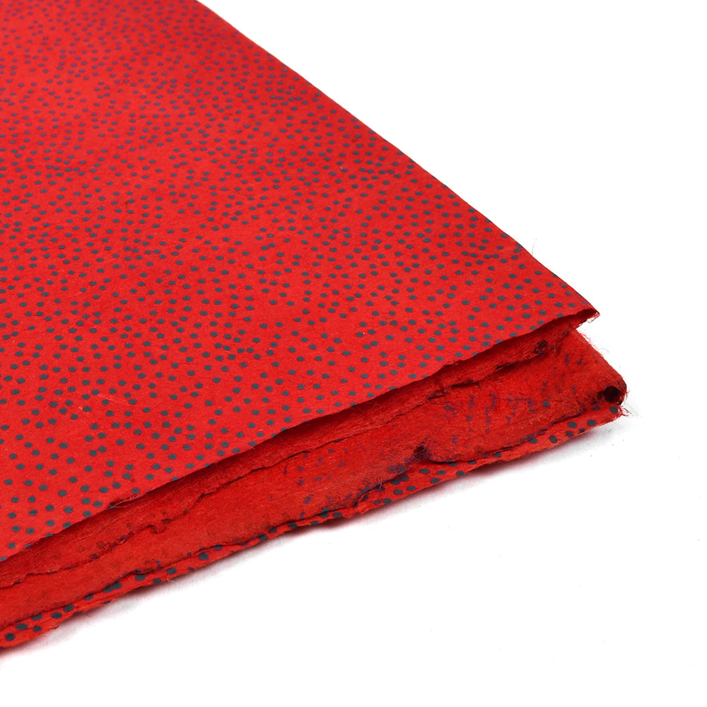 Rotes, handgeschöpftes Nepalpapier mit kleinen schwarzen Punkten, gestapelt mit unregelmäßigen Kanten, aus der Nahaufnahme – eine wunderschöne Wahl für nachhaltiges Papier beim Verpacken von Geschenken.