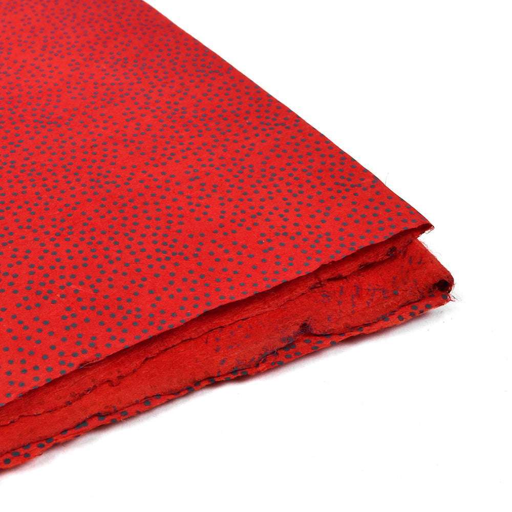 Ein Stapel rotes handgefertigtes Nepalpapier von ☆ mit kleinen schwarzen Tupfen - ideal zum Buchbinden oder liebevoll Geschenke verpacken.