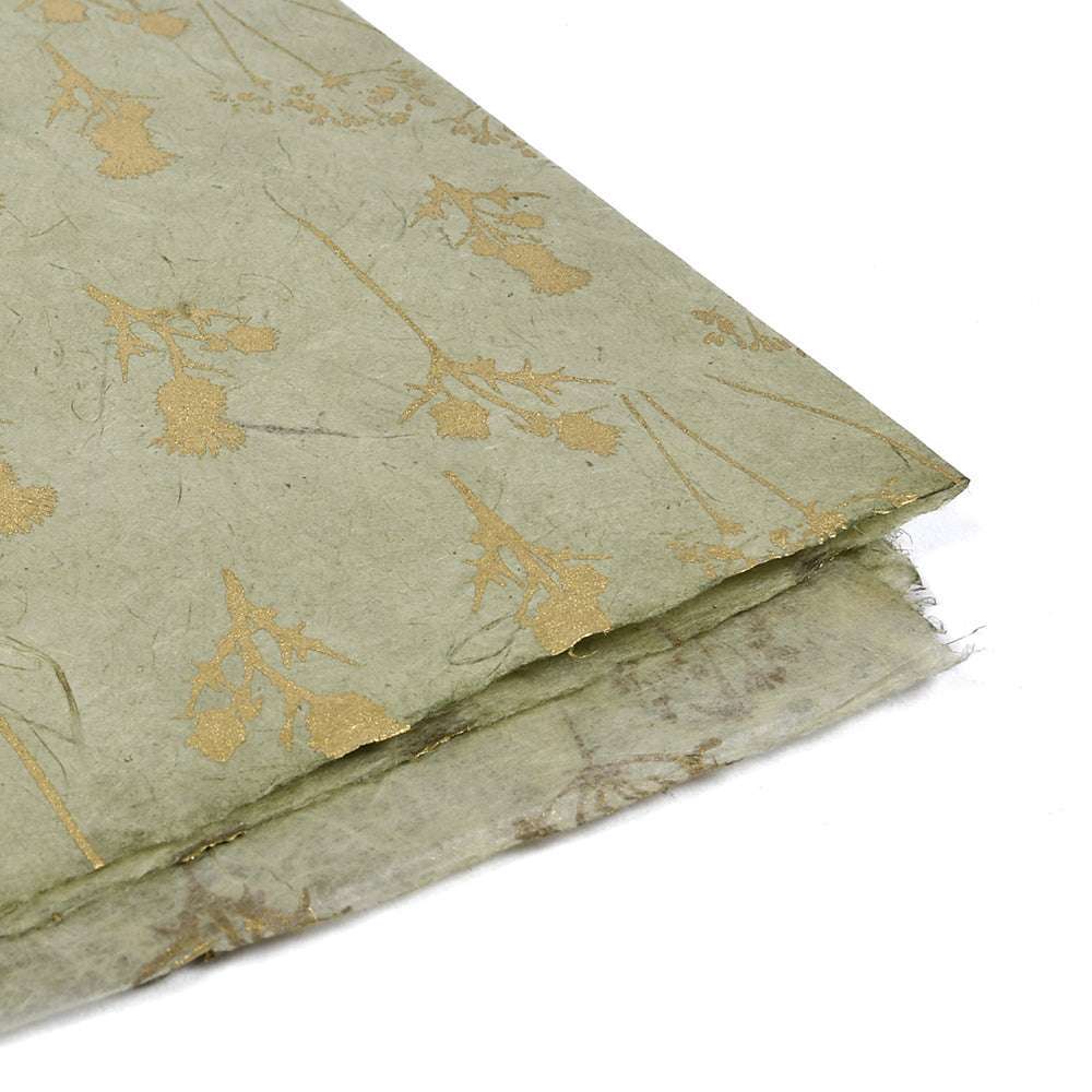 Hellgrünes Nepalpapier mit goldenen Blumenmustern - perfekt für Geschenkverpackungen oder Bucheinbände. Mit strukturierter Oberfläche, gefalteten Ecken und leicht durchscheinenden Rändern.