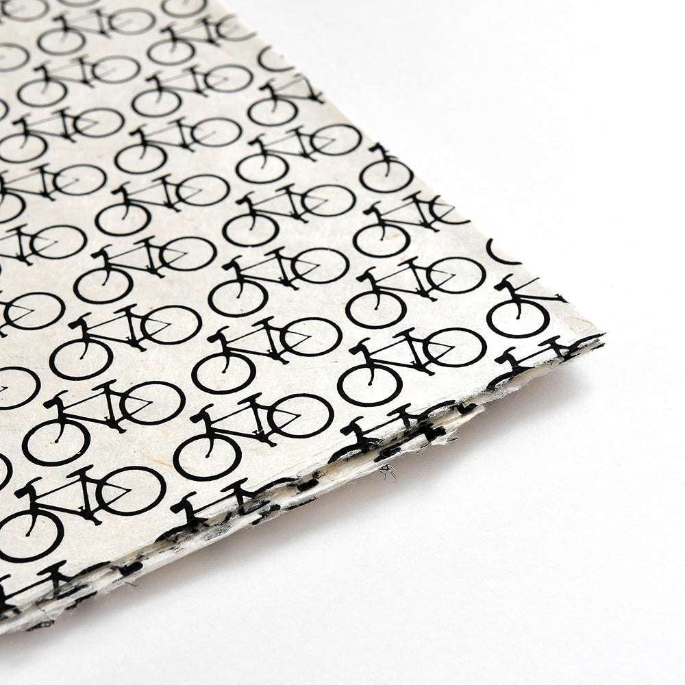 Nahaufnahme von ☆ Nepalpapieren mit einem sich wiederholenden schwarzen Fahrradmuster auf Weiß - ideal für Buchbinden oder stilvolle Geschenkverpackungen.