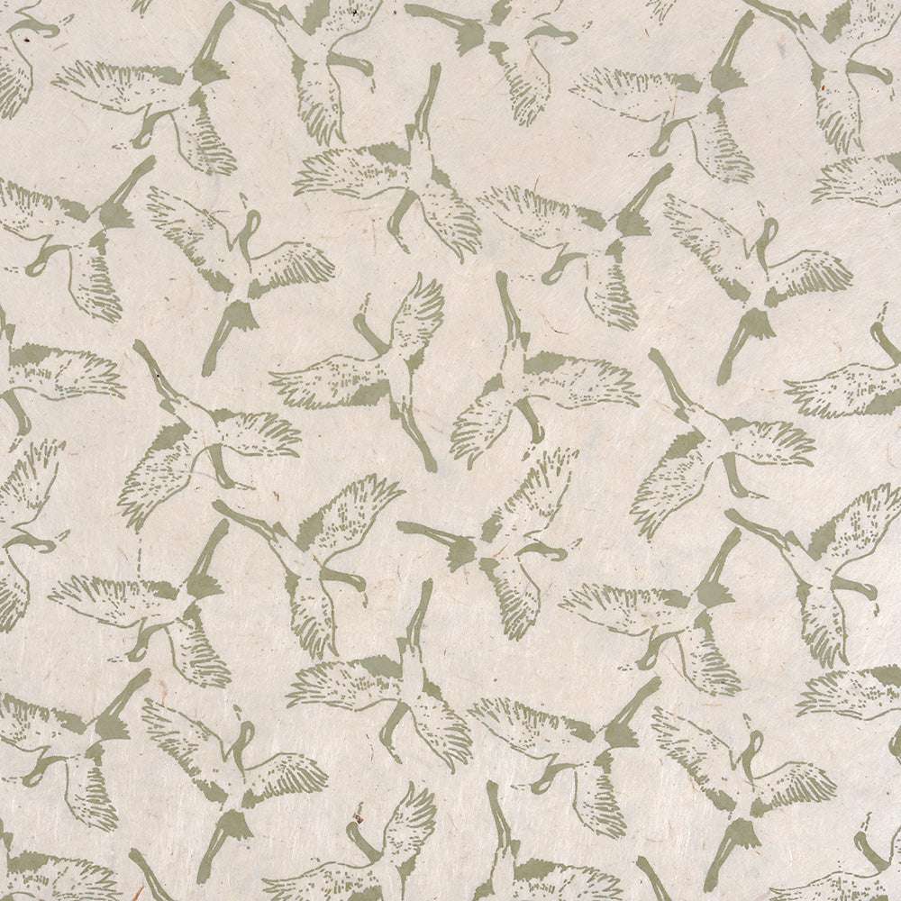 Grüne Kraniche mit ausgestreckten Flügeln schweben über einen beigefarbenen, strukturierten Hintergrund - ideal für Buchbinden oder Geschenkverpackungen mit schönen Nepalpapieren von ☆.