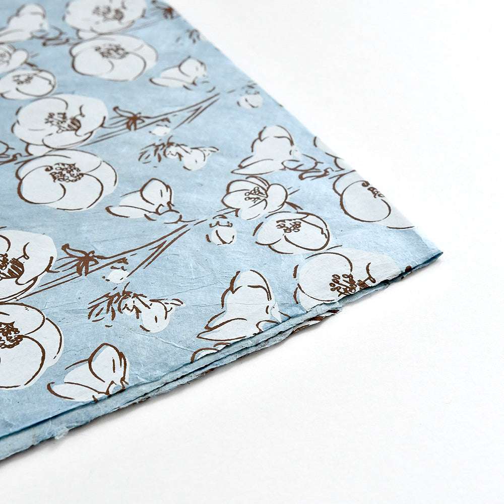 Hellblaues Seidenpapier von ☆ mit weißem und braunem Blumenmuster, an der Ecke auf einer weißen Fläche gefaltet - ideal für Geschenkverpackungen oder Buchbindearbeiten.