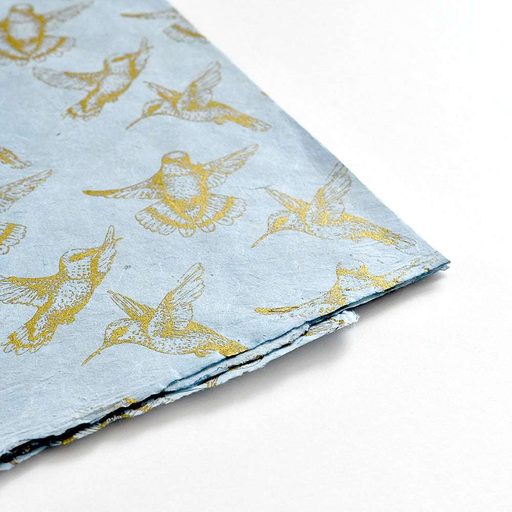 Hellblaue Nepalpapiere von ☆ mit goldenen Kolibri-Illustrationen, ideal für Geschenkverpackungen oder Bucheinbände, fotografiert auf weißem Hintergrund.