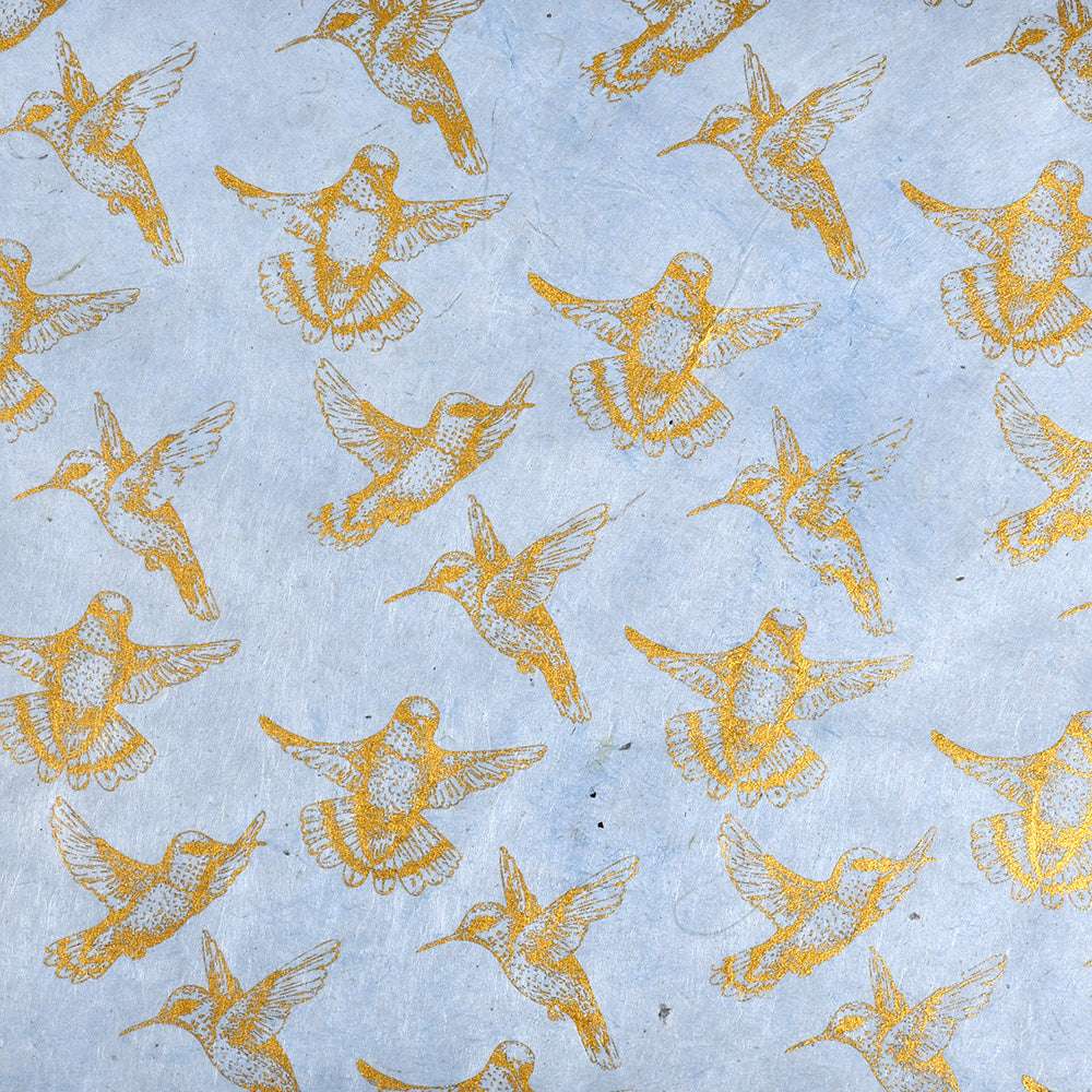 Goldfarbene Kolibriillustrationen auf hellblauem Hintergrund, gleichmäßig verteilt in einem sich wiederholenden Muster - perfekt für Buchbinden oder elegante Geschenkverpackungen in Nepalpapieren ☆.