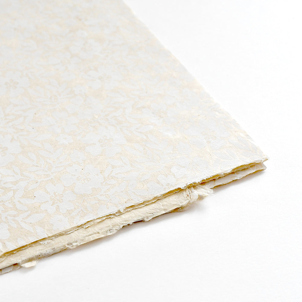 Nahaufnahme von cremefarbenen Nepalpapieren von ☆ mit einem dezenten Blumenmuster - perfekt für Geschenkverpackungen oder Bucheinbände - vor weißem Hintergrund.