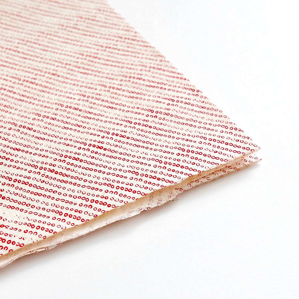 Gefalteter weißer Stoff mit diagonalen Reihen kleiner roter Punkte von ☆, die an Nepalpapiere erinnern - perfekt für Buchbinden oder liebevoll Geschenke Verpacken.