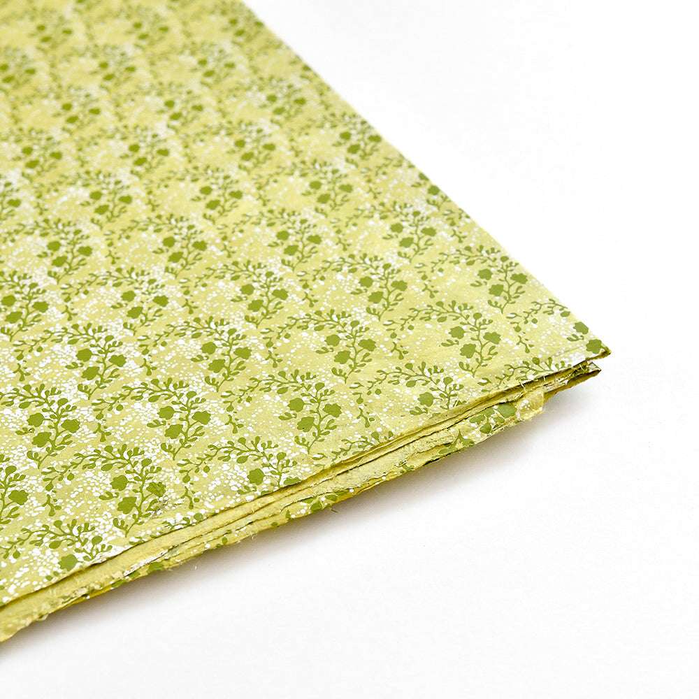 Ein Stapel grün und gelb gemusterter Nepalpapiere von ☆ mit kleinen weißen Blumenmustern, ideal für Buchbinden oder Geschenke Verpacken, dargestellt auf weißem Hintergrund.