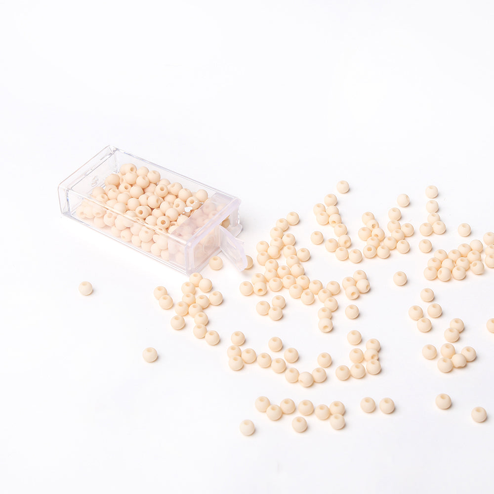 Kleine, runde, beige Acrylperlen von Alexandra Renke quellen aus einer durchsichtigen Box auf eine weiße Fläche - ideal für Schmuck basteln und kreative Bastelprojekte.
