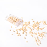 Kleine beige Acrylperlen von Alexandra Renke schwappen aus einem durchsichtigen Plastikbehälter auf eine weiße Fläche - ideal für Schmuck basteln und kreative Bastelprojekte.