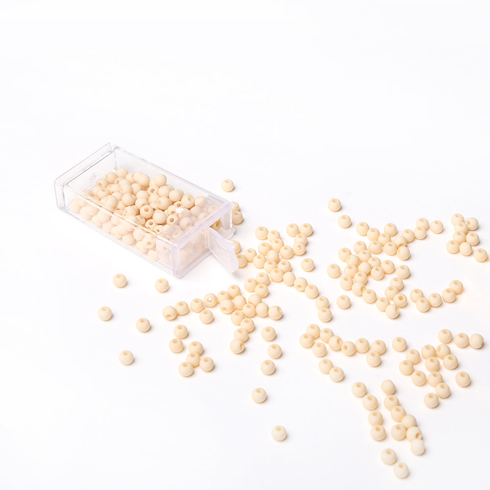 Kleine beige Acrylperlen von Alexandra Renke schwappen aus einem durchsichtigen Plastikbehälter auf eine weiße Fläche - ideal für Schmuck basteln und kreative Bastelprojekte.