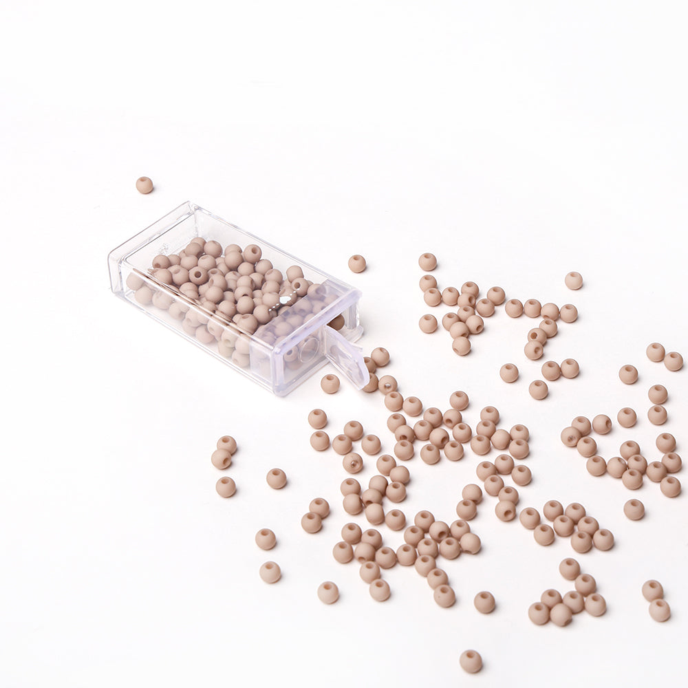Eine klare Kunststoffbox mit hellbraunen, runden Acrylperlen von Alexandra Renke, die auf einer weißen Fläche verstreut sind - ideal für Bastelprojekte oder die Gestaltung individueller Schmuckstücke.