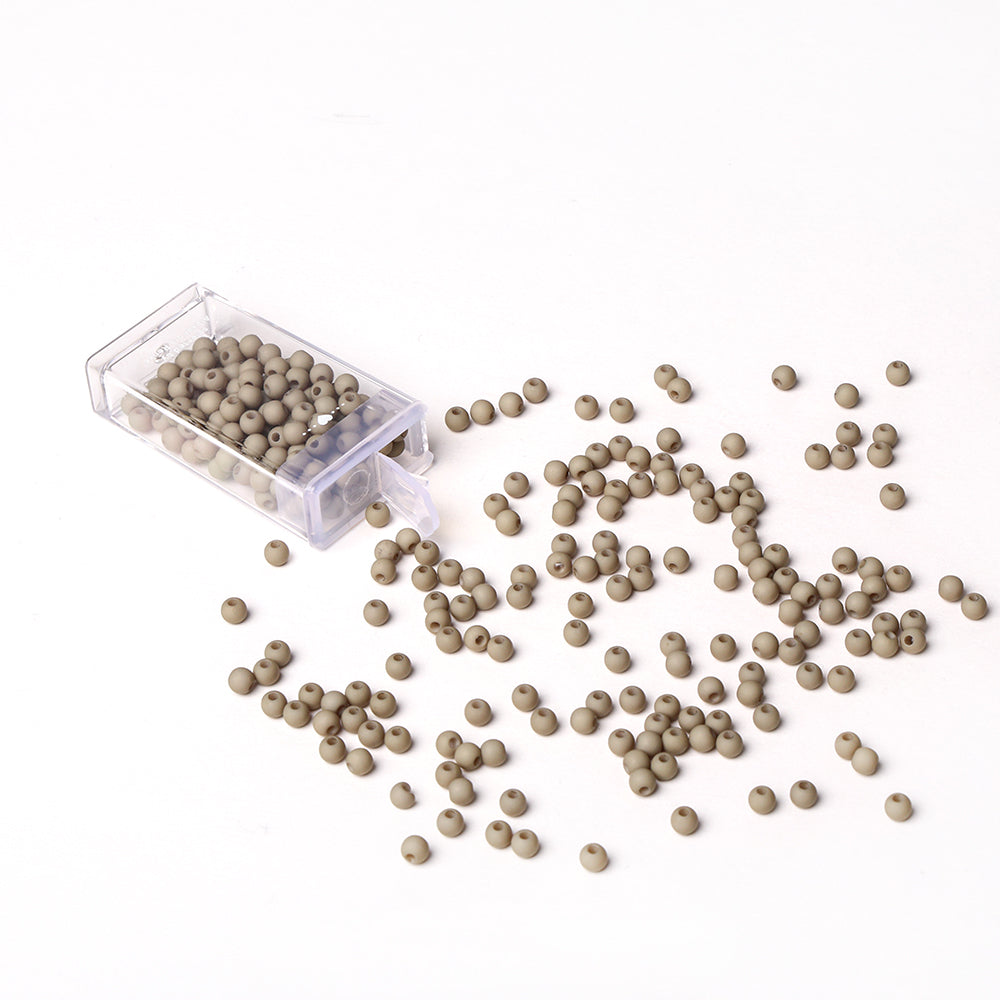 Kleine beigefarbene Acrylperlen von Alexandra Renke aus einem durchsichtigen Plastikbehälter auf eine weiße Fläche geschüttet - ideal für Bastelprojekte oder Schmuck basteln.