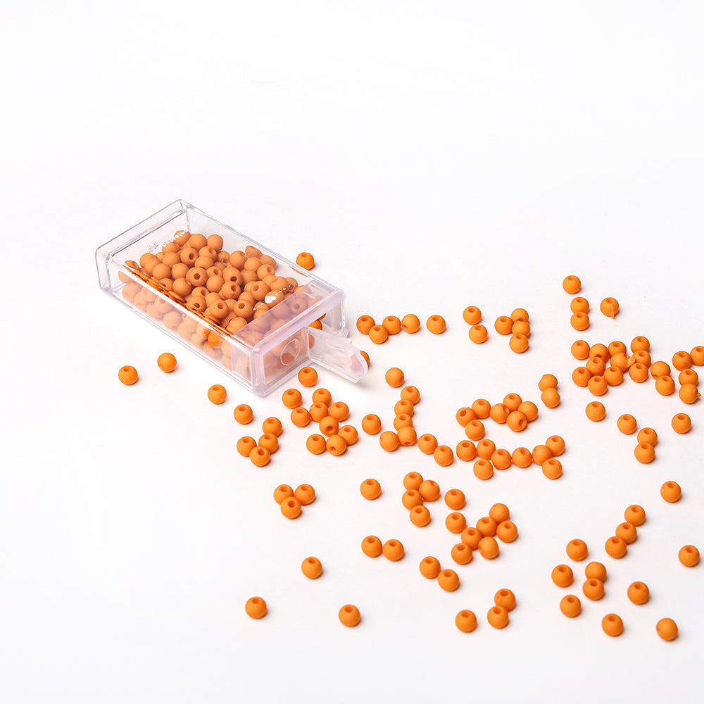 Kleine orangefarbene Acrylperlen von Alexandra Renke ergießen sich aus einem klaren Behälter auf eine weiße Fläche - ideal für Bastelprojekte oder die Herstellung einzigartiger Schmuckstücke.