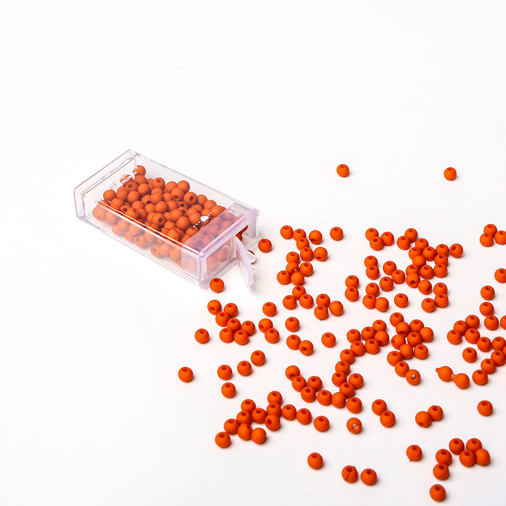 Eine durchsichtige Dose mit orangefarbenen Acrylperlen von Alexandra Renke schwappt auf eine weiße Fläche und verstreut runde Perlen - ideal für Bastelprojekte oder Schmuck basteln.