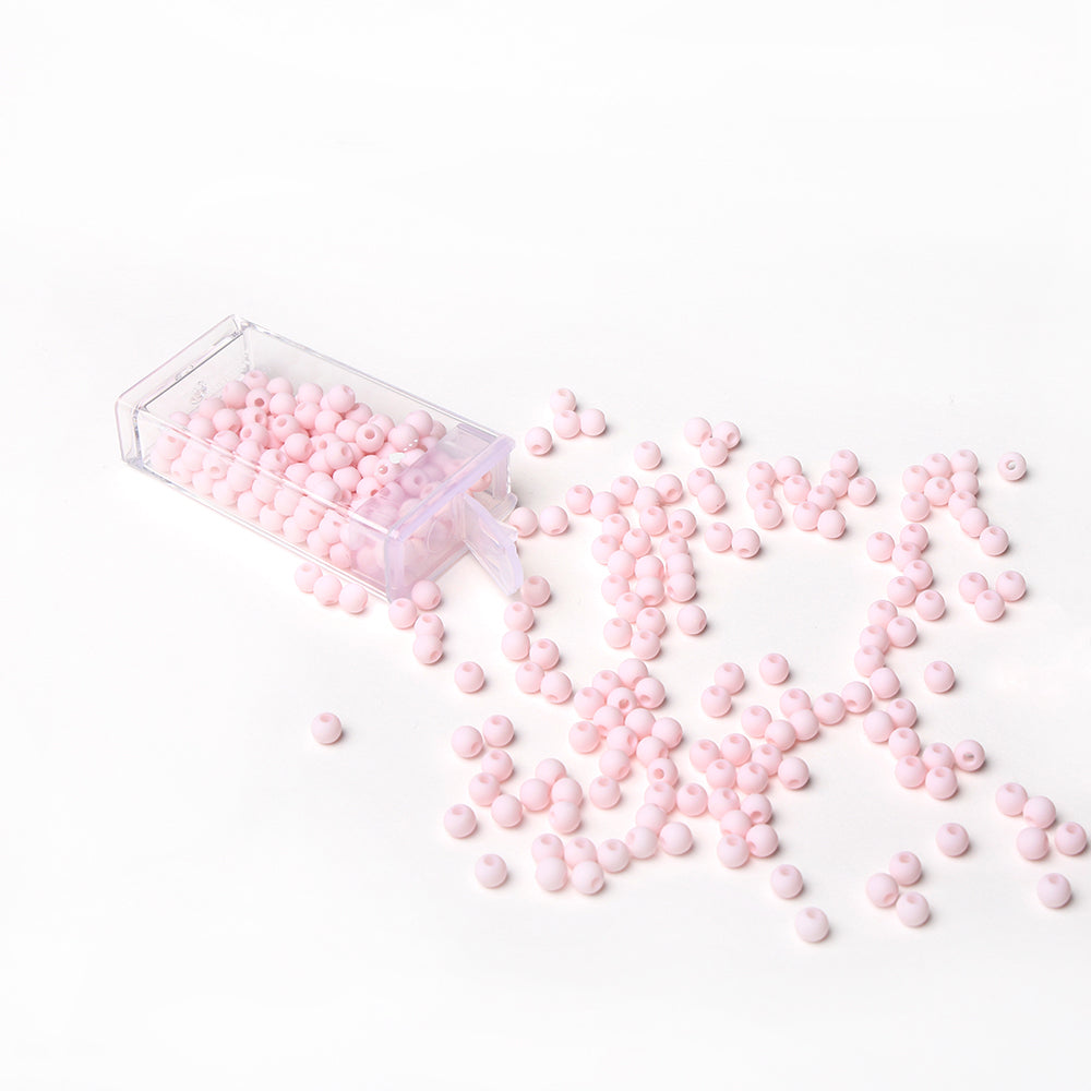 Eine klare Kunststoffbox von Alexandra Renke verschüttet kleine, runde, hellrosa Acrylperlen auf eine weiße Fläche - perfekt für Bastelprojekte oder das Basteln zarter Schmuckstücke.