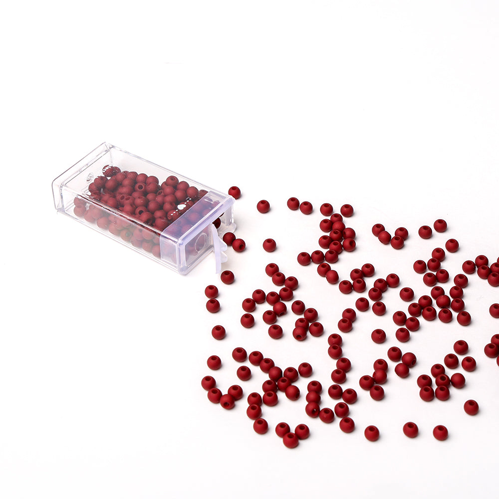 Die kleinen roten Acrylperlen von Alexandra Renke fallen aus einer durchsichtigen Schachtel auf eine weiße Oberfläche - ideal für Bastelprojekte oder die Herstellung von Schmuck.
