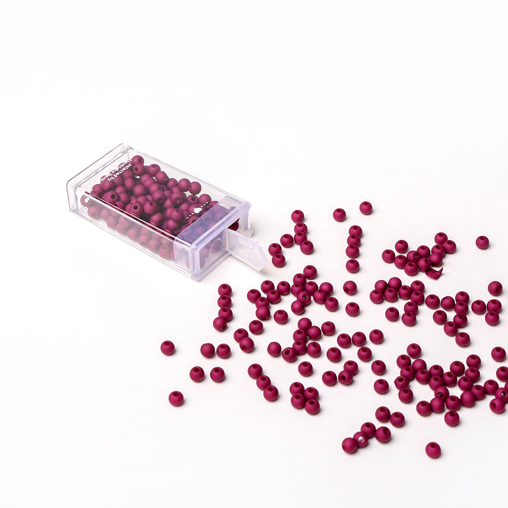 Eine klare Box mit kleinen roten Acrylperlen von Alexandra Renke schwappt auf eine weiße Fläche - ideal für Bastelprojekte oder Schmuckherstellung.