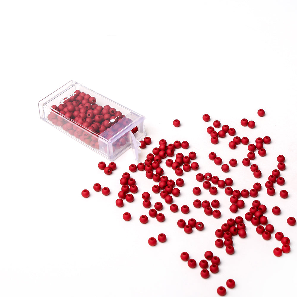 Kleine rote Acrylperlen von Alexandra Renke schwappen aus einer klaren Kunststoffbox auf eine weiße Fläche, perfekt für Schmuckstücke oder kreative Bastelprojekte.