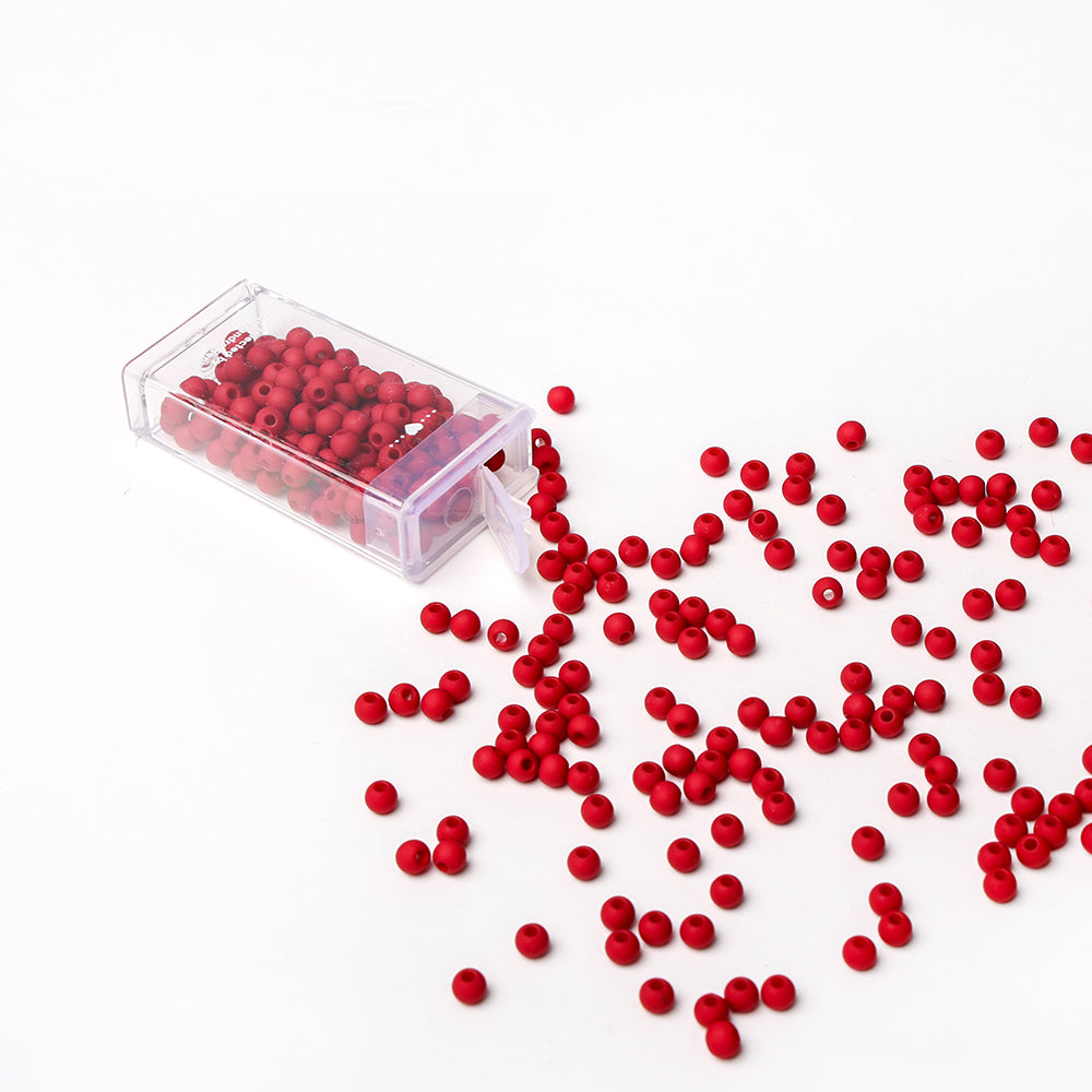 Eine durchsichtige Plastikbox mit roten Acrylperlen von Alexandra Renke ist umgekippt und hat die Perlen auf eine weiße Fläche verschüttet - ideal für Bastelprojekte oder die Herstellung einzigartiger Schmuckstücke.