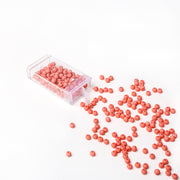 Kleine orangefarbene Acrylperlen von Alexandra Renke schwappen aus einem klaren Kunststoffbehälter auf eine weiße Fläche - ideal für Bastelprojekte und handgefertigte Schmuckstücke.