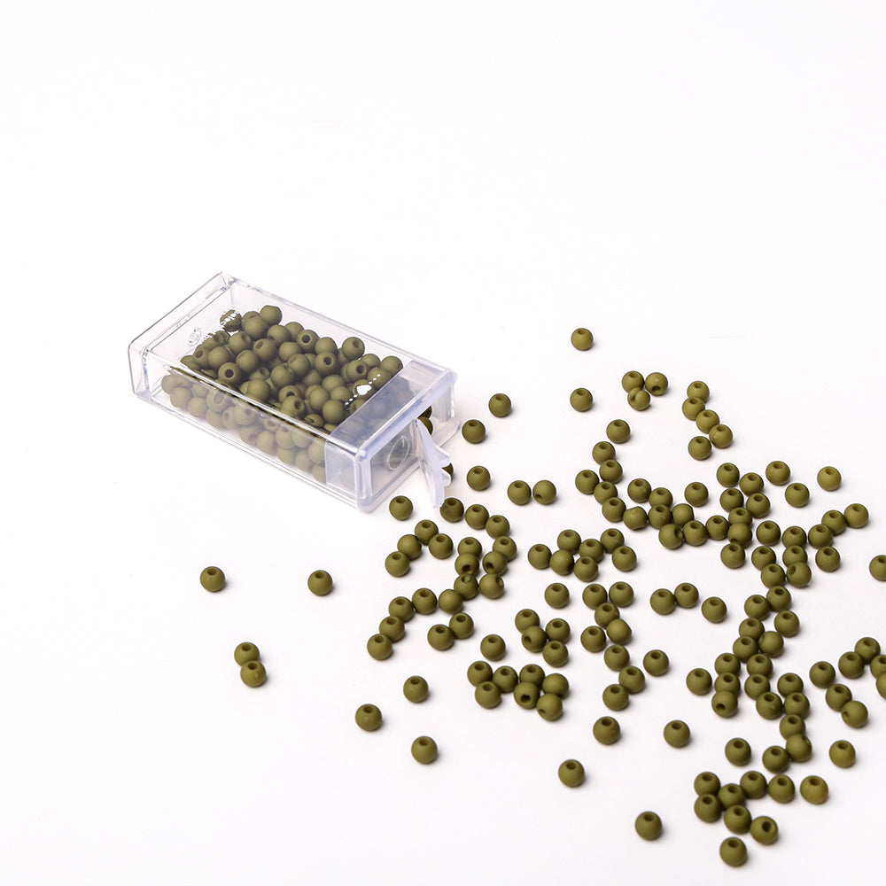 Die kleinen olivgrünen Acrylperlen von Alexandra Renke schwappen aus einem klaren Kunststoffbehälter auf eine weiße Fläche, ideal für Schmuck basteln und kreative Bastelprojekte.
