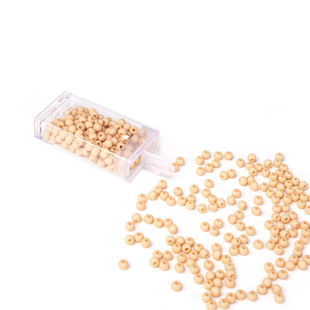 Kleine beige Acrylperlen von Alexandra Renke schwappen aus einem durchsichtigen Kunststoffbehälter auf eine weiße Fläche - ideal für Bastelprojekte oder Schmuck basteln.