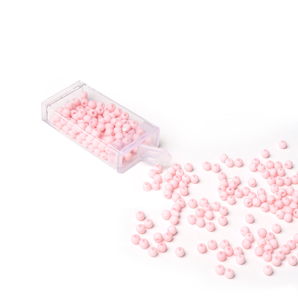 Eine durchsichtige Schachtel mit kleinen rosafarbenen Acrylperlen von Alexandra Renke, ideal zum Schmuck basteln, mit einigen verstreuten Perlen auf weißer Oberfläche - ein Muss für Ihre Bastelzubehör-Sammlung.