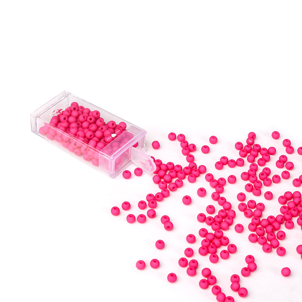 Kleine rosa Acrylperlen von Alexandra Renke schwappen aus einem klaren Behälter auf eine weiße Fläche, ideal für Bastelprojekte oder Schmuck basteln.