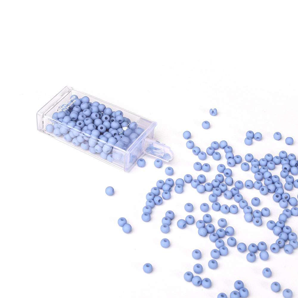Kleine, runde, hellblaue Acrylperlen von Alexandra Renke schwappen aus einem klaren Kunststoffbehälter auf eine weiße Fläche - ideal für Bastelprojekte oder Schmuck basteln.