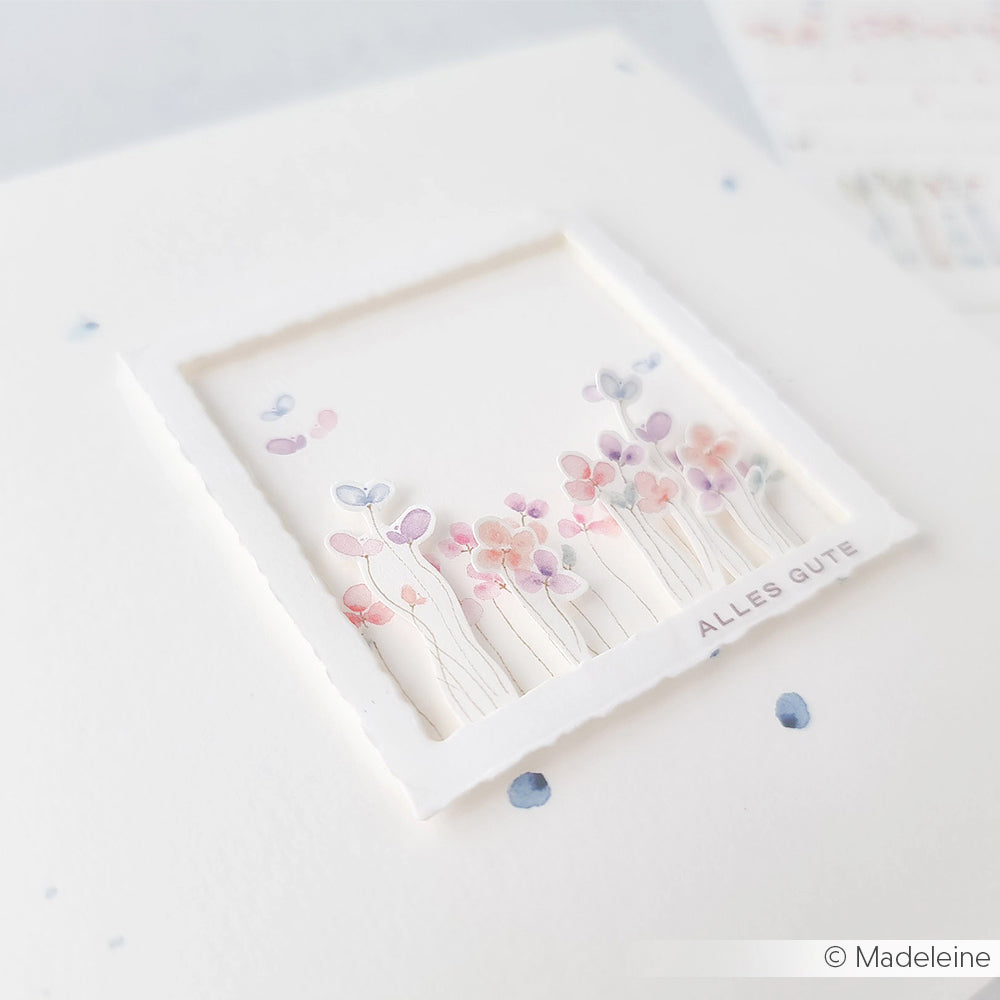 Zarte Aquarellblumen und Schmetterlinge umrahmen ALLES GUTE in einem weißen Quadrat auf einer Karte, die mit der Motivstanze Büttenrand Quadrat von Alexandra Renke und hochwertigen Designpapieren eine elegante Note erhält.