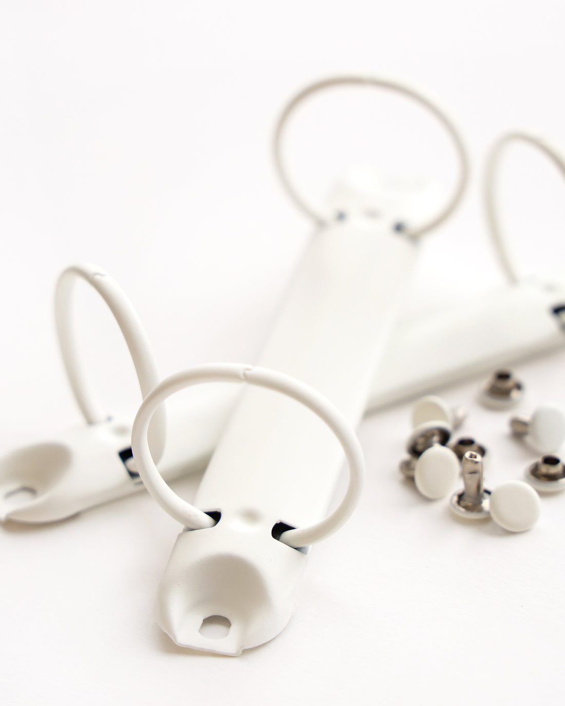 Nahaufnahme von weißen Binderingen und Metallverschlüssen auf weißem Hintergrund.