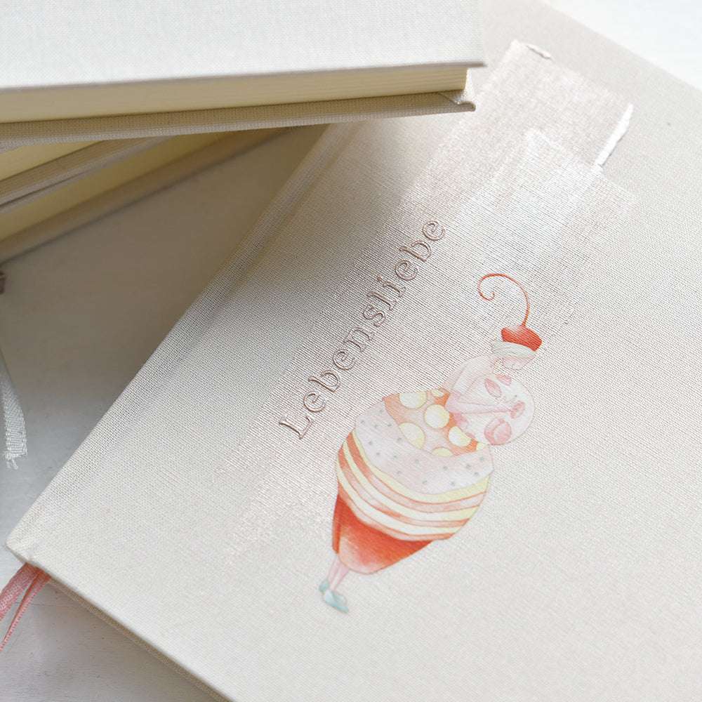 Ein beigefarbenes Alexandra Renke Notizbuch mit "Lebensliebe" und einer skurrilen Dessert-Illustration - perfekt zur Inspiration für Bastelprojekte Motive oder Rub-On Figurenwelt Kreationen.