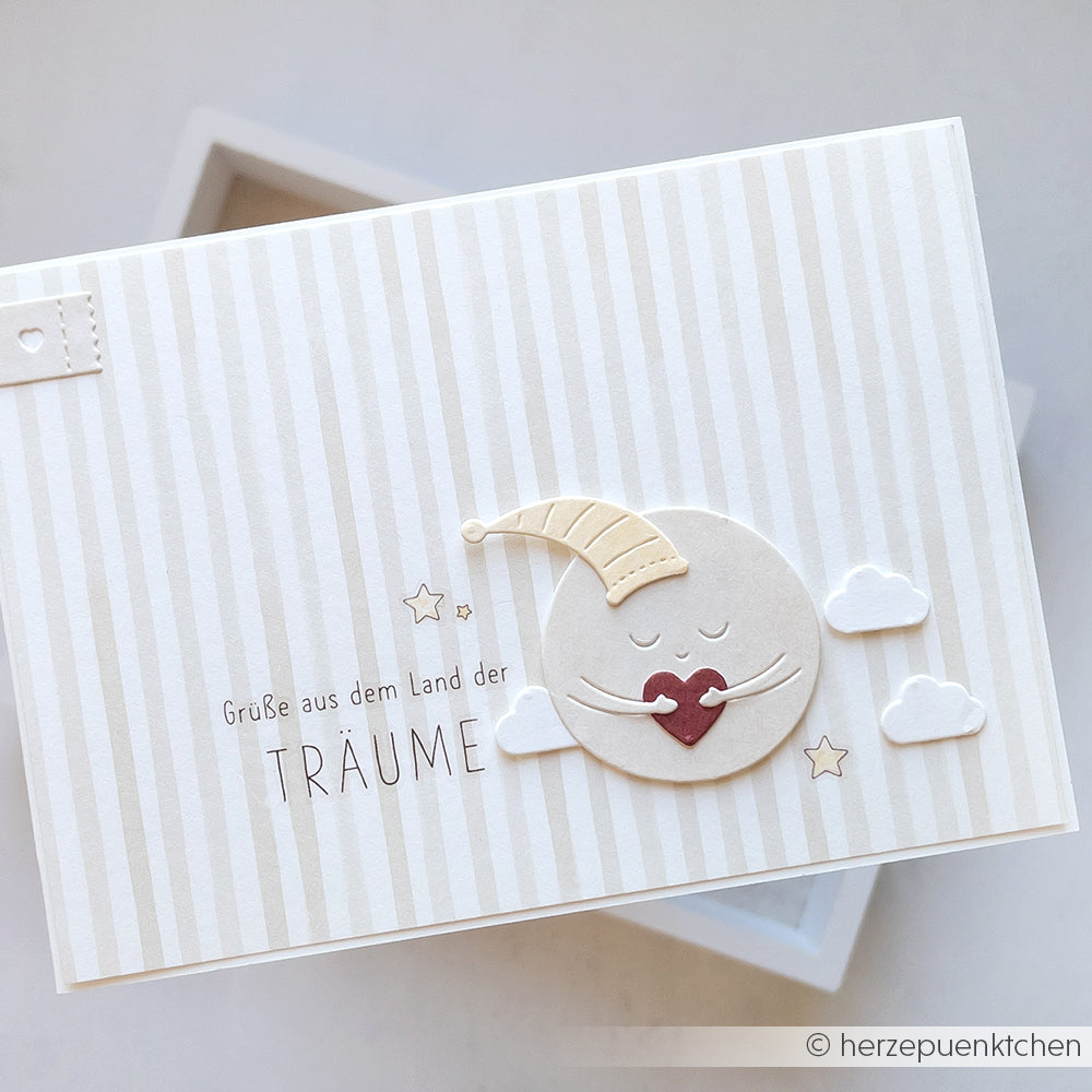 Grußkarte von Alexandra Renke mit einem lächelnden Mond in einer Nachtmütze, Wolken, Sternen und deutschem Text auf Streifen - ideal für Bastelprojekte oder zur kreativen Gestaltung mit Rub-On Babyfreude.