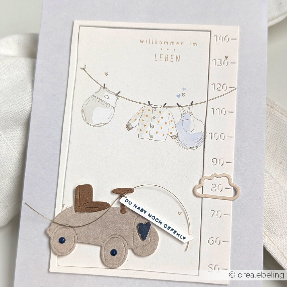 Diese Babykarte von Alexandra Renke zeigt Kleidung auf einer Leine, ein Spielzeugauto und einen deutschen Begrüßungstext - ideal, um mit Rub-On-Motiven oder Transferfolien Basteln eine kreative Note hinzuzufügen.