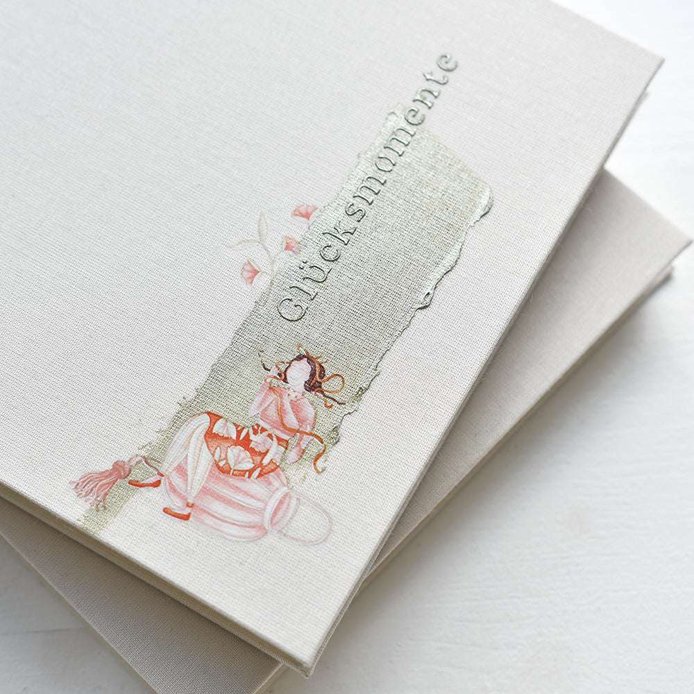 Beigefarbenes Albumcover von Alexandra Renke mit einer Mädchen- und Blumenillustration, silberner Glücksmomente-Text - ideal für Bastelprojekte Motive oder in Kombination mit Rub-On Figurenwelt für eine einzigartige Note.