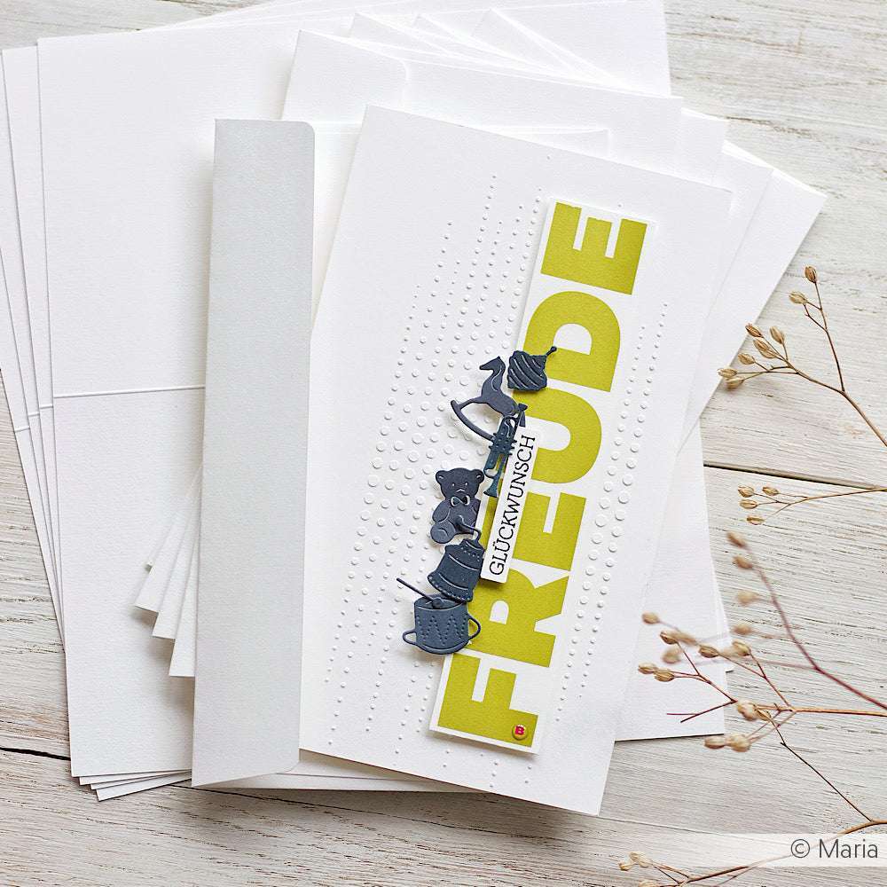 Eine weiße Alexandra Renke Grußkarte mit FREUDE in fetten grünen Buchstaben und dekorativen Akzenten, ideal für Bastelprojekte Motive oder passend zu Rub-On Happy Words, ruht auf einem Stapel Umschläge.