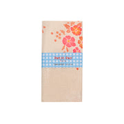 Beigefarbene Baumwollserviette mit orange-rosa Blumenmuster, aus beschichtetem Stoff für eine wasserabweisende Oberfläche, gefaltet und mit einem blauen Petit-Pan-Etikett umwickelt.
