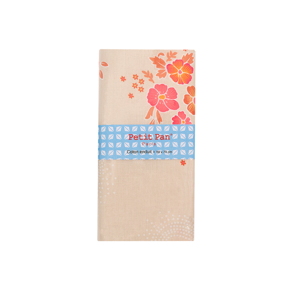 Beigefarbene Baumwollserviette mit orange-rosa Blumenmuster, aus beschichtetem Stoff für eine wasserabweisende Oberfläche, gefaltet und mit einem blauen Petit-Pan-Etikett umwickelt.
